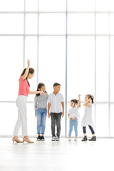 Asian woman and little Asian girl raise their one's hand among Asian kids in front of big white window.
