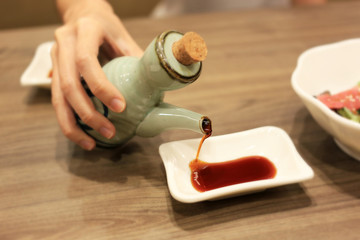 Hand holding pottery soy sauce (Shoyu) pouring to white dish. Shoyu dipping sauce for eat japanese food.