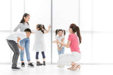 Naklejka premium Asian woman in pink shirt playing something with Asian boy ans girls, they stand in front of big white window.