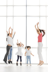 Asian woman in pink shirt playing something with Asian boy ans girls, they jump together, they stand in front of big white window.