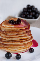 Stack of american pancakes with blackcurrant jam and fresh blackcurrant berries are lying on a white plate.
