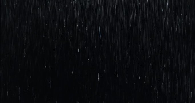 Heavy rain wall falling in front of the camera against black screen. Raindrops splashing. Rain closeup vfx insert. Practical seamlessly loopable footage. Heavy rainstorm hitting black surface.