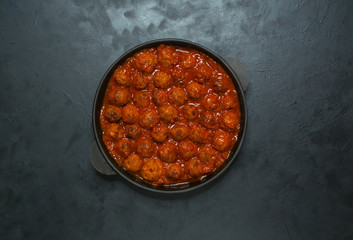 Tender glazed meatballs in a frying pan on a black table.