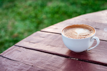 Latte coffee in cup on wooden table and lawn