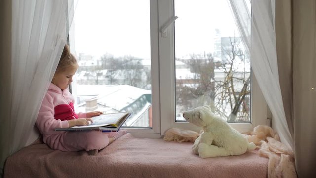 Little girl sits on the windowsill and reads