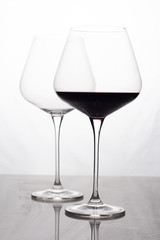 two glass glasses empty and with red wine on a white background.