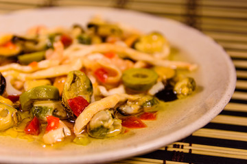 Ceramic plate with different sea food and olives on a bamboo mat