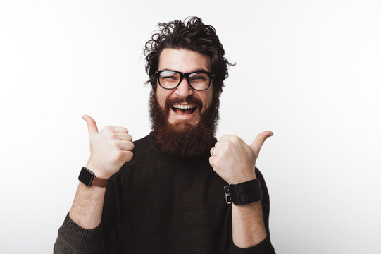 Cheerful bearded man in casual wearing glasses and showing thumbs up over white background