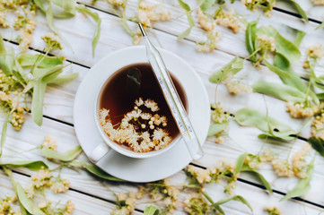 The concept of herbal medicine. A mercury glass thermometer lies on a white cup with a linden, fragrant healing tea made from dried linden flowers on a grey wooden background.