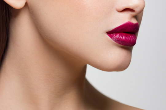 Cosmetics, makeup and trends. Bright lip gloss and lipstick on lips. Closeup of beautiful female mouth with pink lip makeup. Beautiful part of female face. Perfect clean skin in pink light