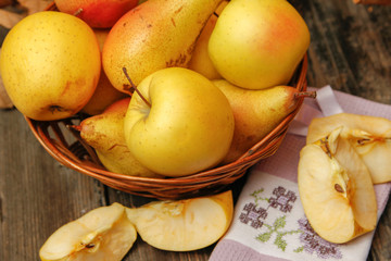 Fresh raw organic pears and apples in a basket on rustic wooden table. Close-up.