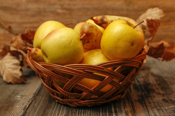 Fresh raw organic pears and apples in a basket on rustic wooden table. Close-up.