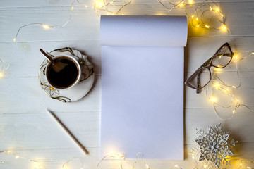 A cup of coffee, an album and decorations on a white wooden table. Background with copy space.