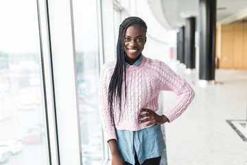 Young casual afro american woman standing in front of panoramic window in modern business center