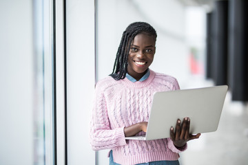 Young beauty afro american student woman holding open laptop on panoramic windows University background.