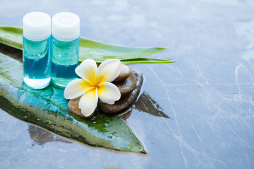 Fototapeta na wymiar spa objects and stones, flower and bottles for massage treatment on dark background.