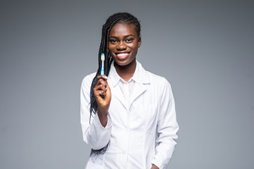 Beautiful african female dentist doctor holding and showing a toothbrush isolated on a gray...