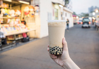 A young woman is holding a plastic cup of brown sugar bubble milk tea at a night market in Taiwan, Taiwan delicacy, close up.