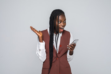 Portrait of shocked young african woman holding mobile phone over gray background