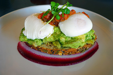 Multigrain avocado toast with poached eggs on top and beet coulis