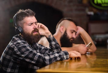 Order drinks at bar counter. Men with headphones and smartphone relaxing at bar. Avoid...