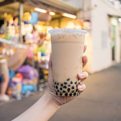 A young woman is holding a plastic cup of brown sugar bubble milk tea at a night market in Taiwan, Taiwan delicacy, close up.