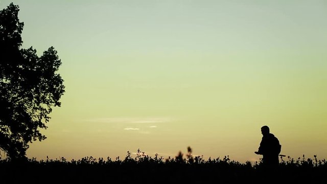 Hunter at sunset stands with a gun on his shoulder