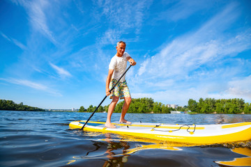 Happy man is paddling on a SUP board