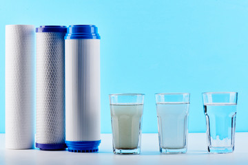 Water filters concept. Carbon cartridges and a three glasses on a white blue background. Household...