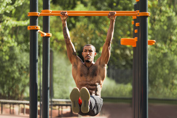 African-american man doing L-sit on horizontal bars