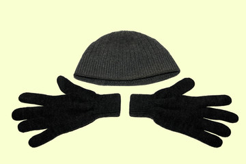 A pair of grey winter knitted gloves and a grey winter hat. On yellow background. The view from the...