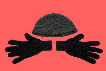 A pair of grey winter knitted gloves and a grey winter hat. On red background. The view from the...