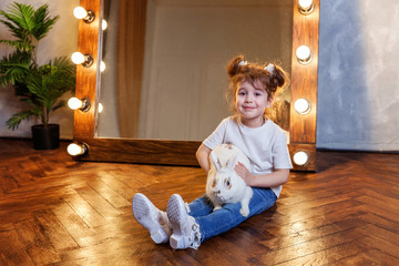 Easter celebration, pet care and animals concept. Cute happy little girl sitting on floor, holding...