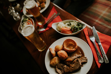 Sunday roast meal with beef, vegetables and beer, with dark light.
