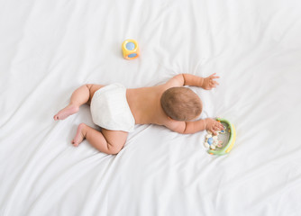 Small baby with lying on his belly with toys