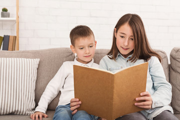 Brother and sister reading book on sofa