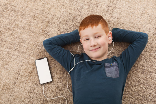 Boy enjoy music. Kid in headphones lying on floor indoors