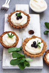Mini tarts (tartlets) with whipped cream or custard and fresh berries served with mint. Homemade dessert. Grey background. Copy space.