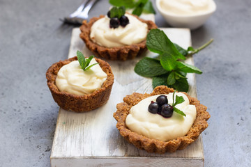 Mini tarts (tartlets) with whipped cream or custard and fresh berries served with mint. Homemade dessert. Grey background. Copy space.