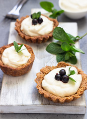 Mini tarts (tartlets) with whipped cream or custard and fresh berries served with mint. Homemade dessert. Grey background. Copy space.