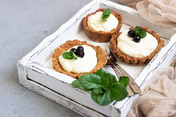 Mini tarts (tartlets) with whipped cream or custard and fresh berries served with mint. Homemade dessert. Grey background. Copy space.