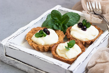 Mini tarts (tartlets) with whipped cream or custard and fresh berries served with mint. Homemade dessert. Grey background. Copy space.