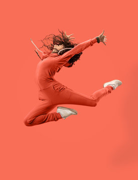 Freedom in moving. Mid-air shot of pretty happy young woman jumping and gesturing against coral studio background. Runnin girl in motion or movement. Human emotions and facial expressions concept