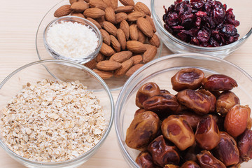 Ingredients for energy bites: nuts, dates, coconut flakes, oatmeal with a food processor on a wooden background.
