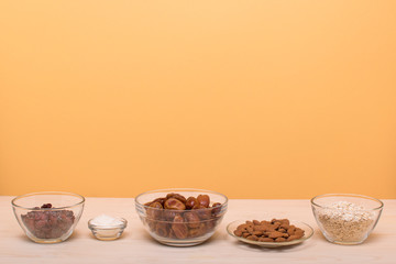 ngredients for energy bites: nuts, dates, coconut flakes, cranberry oatmeal on a warm yellow background.