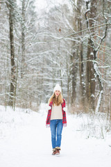 Fototapeta na wymiar Young happy woman in winter clothes walks in the snowy forest
