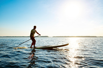 Fototapeta na wymiar Joyful guy paddling on a SUP board