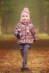 Child girl walking on a pathway in a autumn forest. Winter wear and fashion and empty copy space for Editor's text.