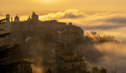 Fototapeta premium Bergamo, one of the most beautiful city in Italy. Lombardy. Amazing landscape of the fog rises from the plains and covers the old town at sunrise