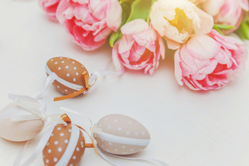 Obraz na płótnie Canvas Spring greeting card. Easter eggs with moss cotton and pink fresh tulip flowers bouquet on rustic white wooden background. Easter concept. Flat lay top view copy space. Spring flowers tulips
